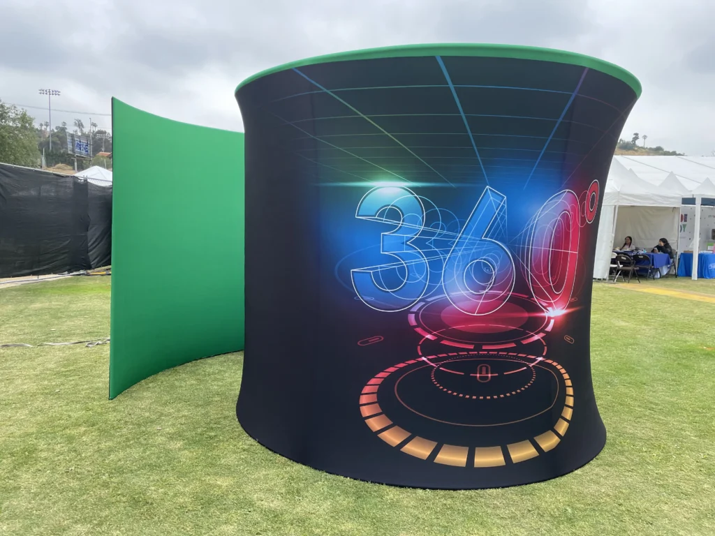 Large outdoor 360 degree event booth installation with graphic display and green screen.