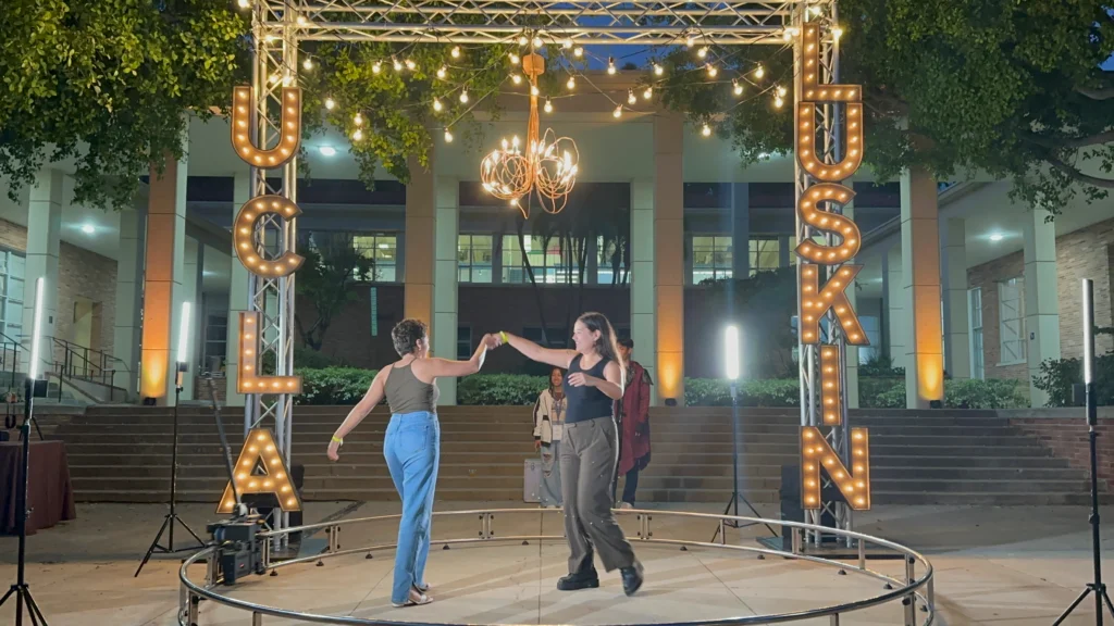 Participants dance on a 360 photo booth at a UCLA Luskin outdoor event under lights.