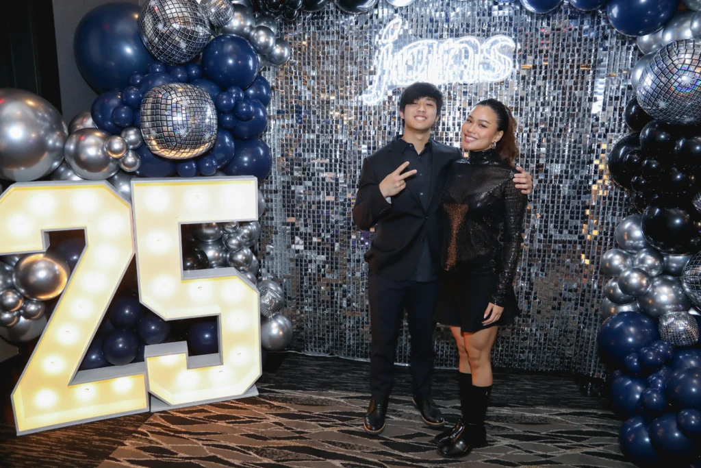 Couple celebrating at a 25th-anniversary event photo booth with lighted props.