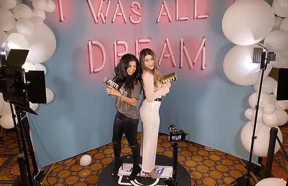 Two women enjoying a fun photo booth experience with party props at a blog-worthy event.