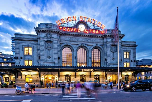 Evening view of Denver's Union Station illuminated with people and vehicles outside.