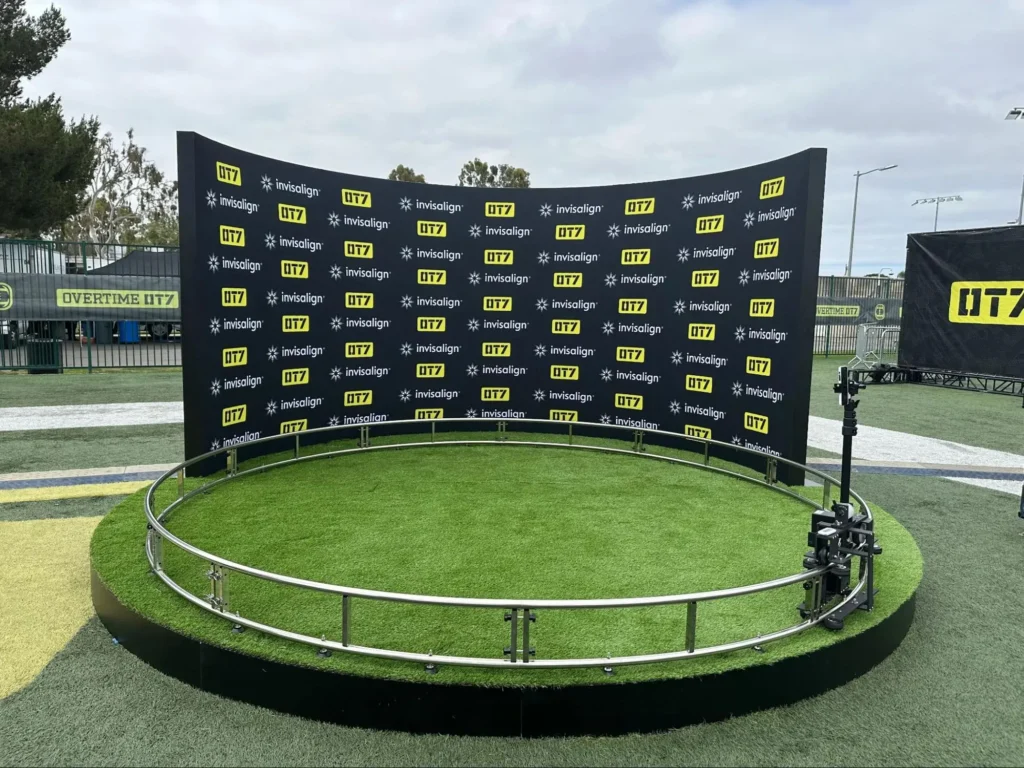 Empty 360 photo booth setup on grass with branded banners, ready for event.