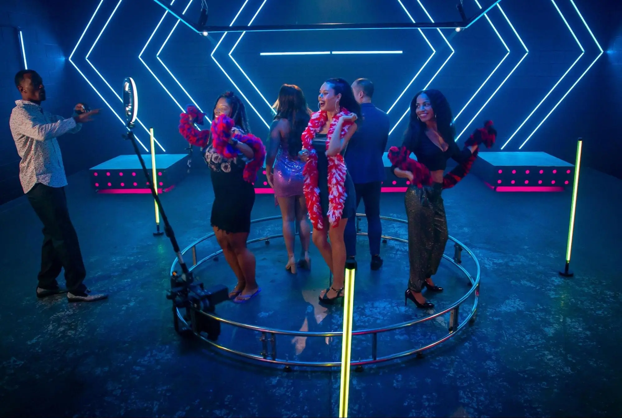 Group dancing inside a neon-lit 360 photo booth at lively party.