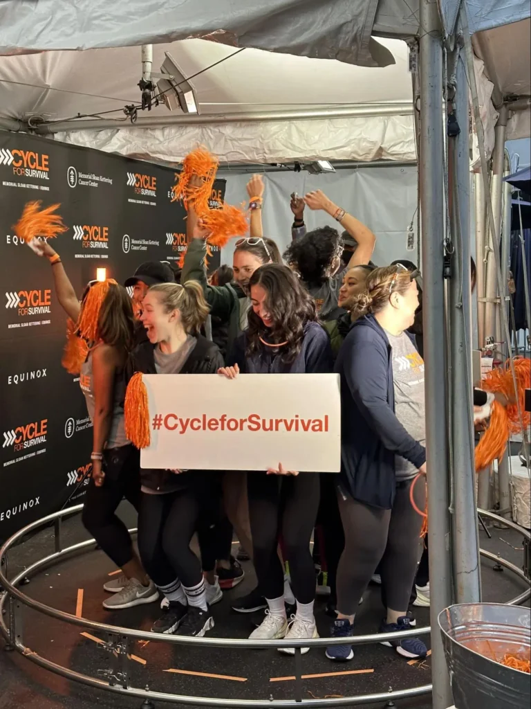 Group of participants holding sign 'Cycle for Survival' on 360 photo booth at charity event.