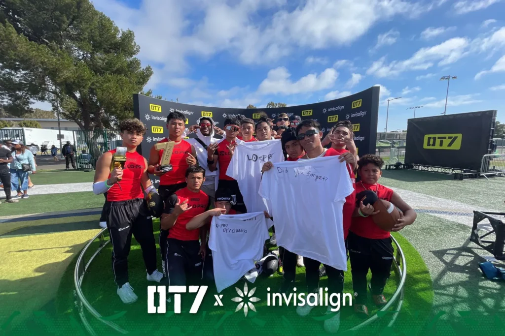 Group of young athletes on 360 photo booth platform holding trophies and T-shirts at sports event.