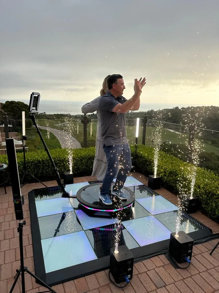 Man using 360 photo booth with spark effect, overlooking coastal landscape.