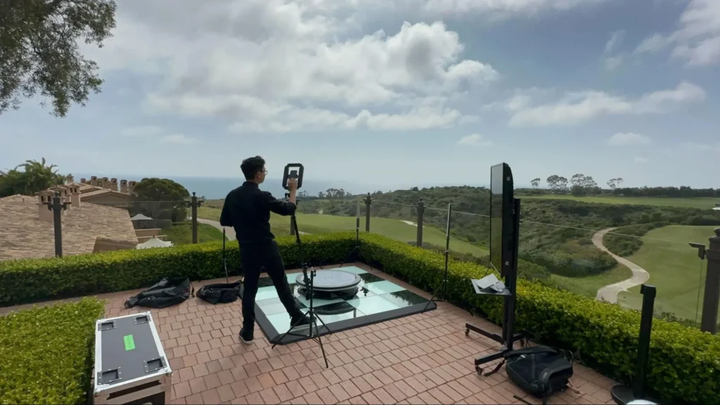 Technician setting up a 360 photo booth on a terrace overlooking a scenic golf course.