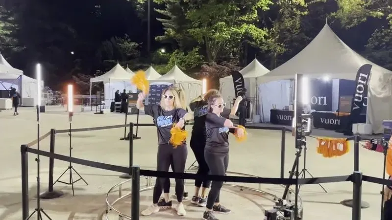 Two women cheerleading on 360 photo booth at night event with vibrant lighting.