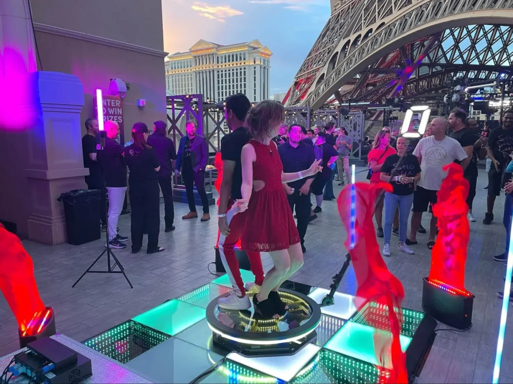 Young woman dancing on 360 photo booth platform at outdoor event with vibrant lighting.