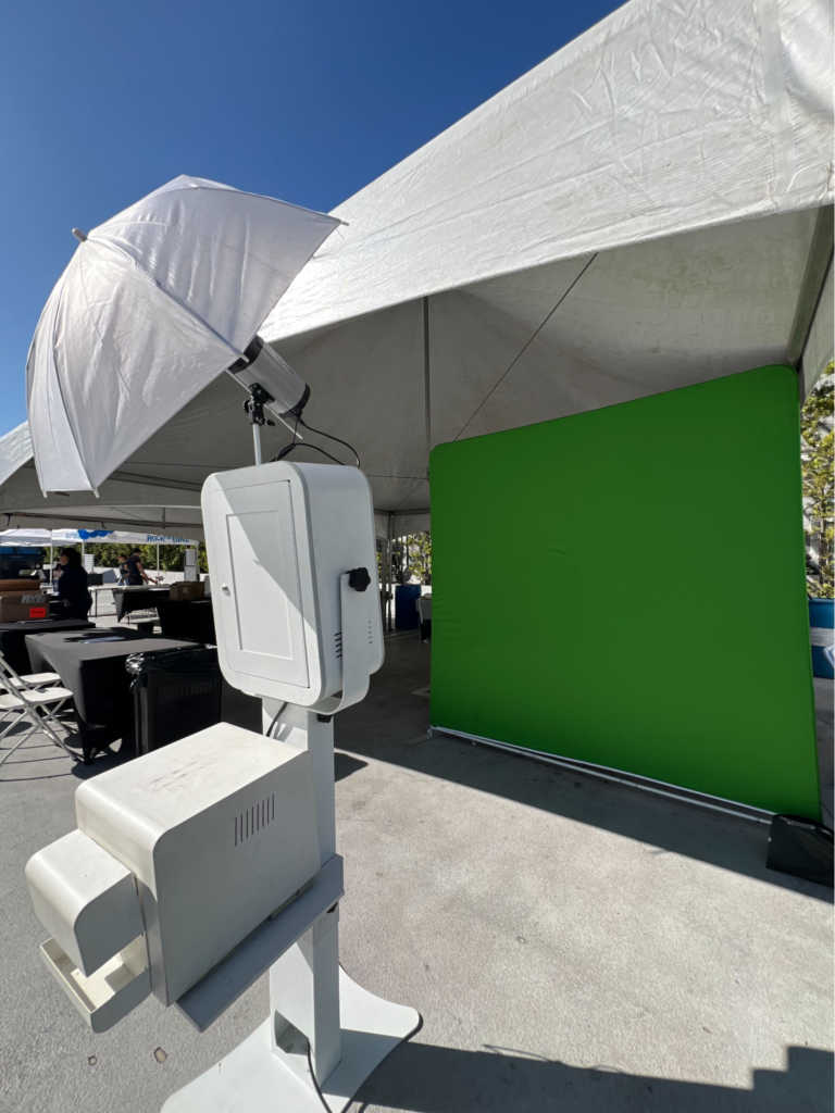 Outdoor corporate photo booth with green screen setup under white canopy.