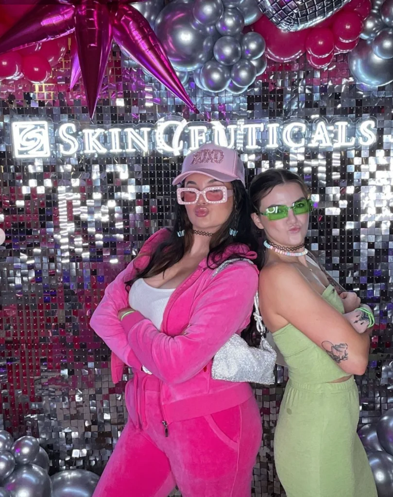 Two women posing in a Skinceuticals branded glam photo booth with reflective background.