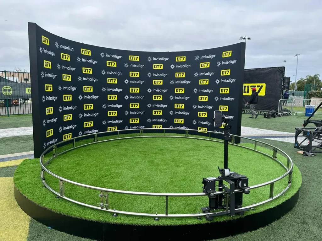 360-degree photo booth setup with branded backdrop and green grass platform.