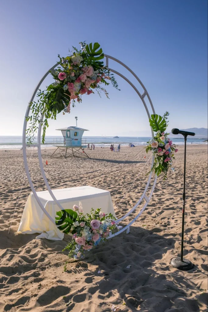 Beach wedding arch with floral decor and microphone stand.