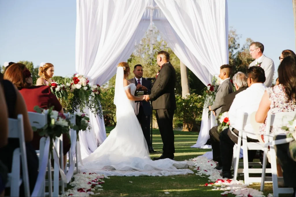 Bride and groom exchanging vows under a draped outdoor arch.