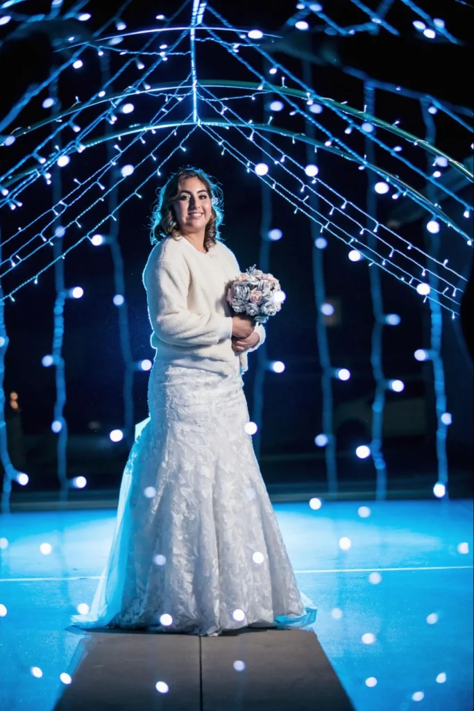 Bride smiling under blue lights holding her bouquet.