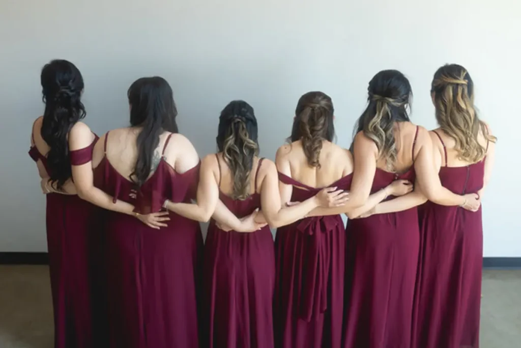 Bridesmaids in burgundy dresses posing with backs turned showing matching hairstyles