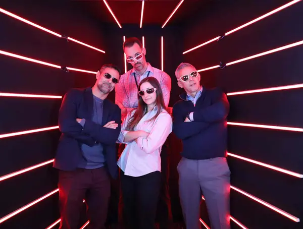 Group of four professionals posing confidently in a dynamic event setting with vibrant red neon lights, showcasing a stylish and modern corporate vibe.