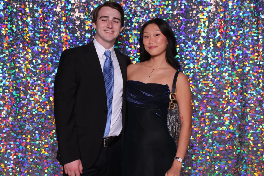 Couple in formal attire posing in front of a vibrant, colorful confetti backdrop, capturing a festive and glamorous photo booth moment