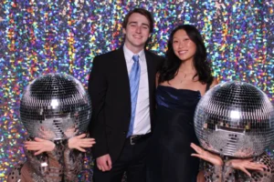 Couple posing with disco ball props in a colorful photo booth setup at a party.