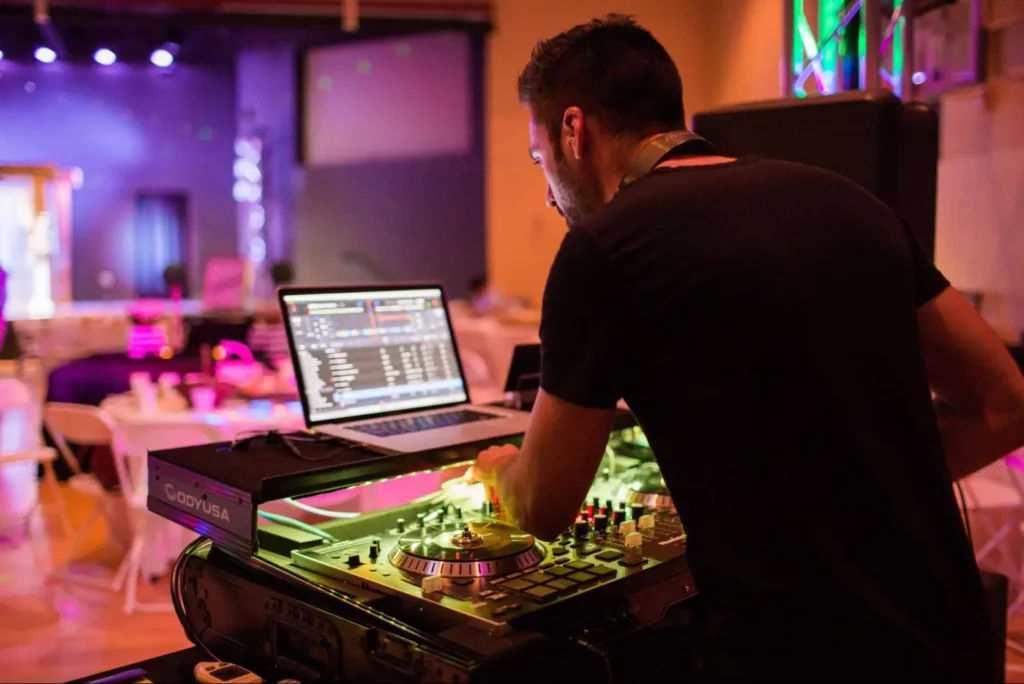 DJ using a laptop and professional sound equipment at an event.