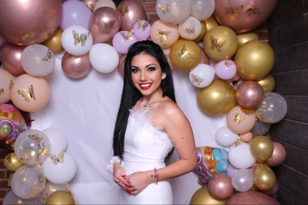 Elegant woman in a white dress posing in front of a stunning balloon backdrop.