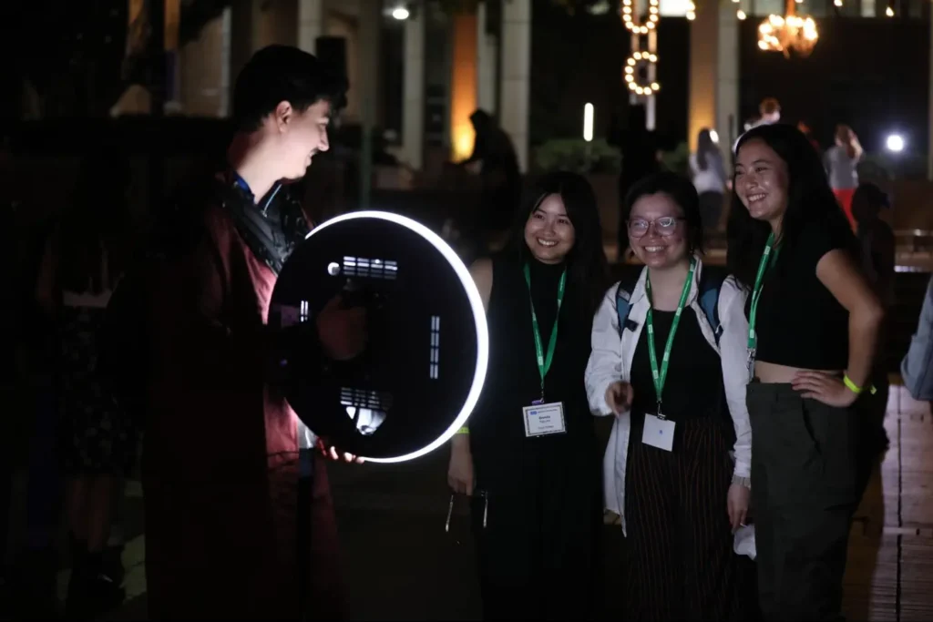 Event attendees interact with a ring light setup during a nighttime event.