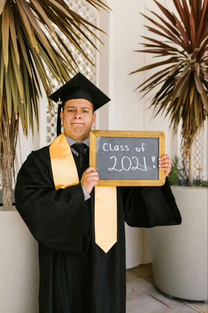 Graduate posing with a chalkboard that says Class of 2021 in a stylish, modern setting.