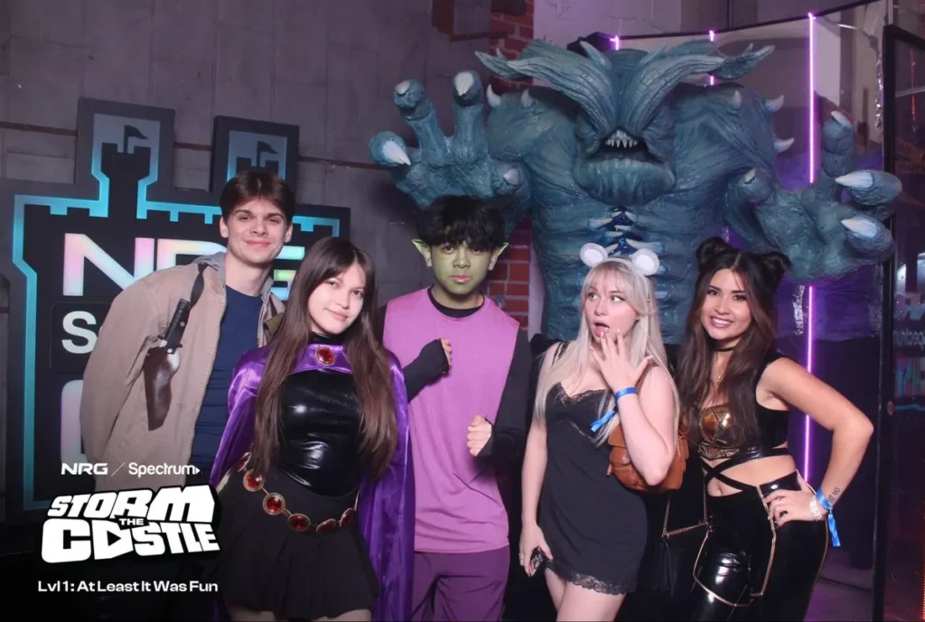 Group in cosplay poses at a themed event with a giant monster backdrop.