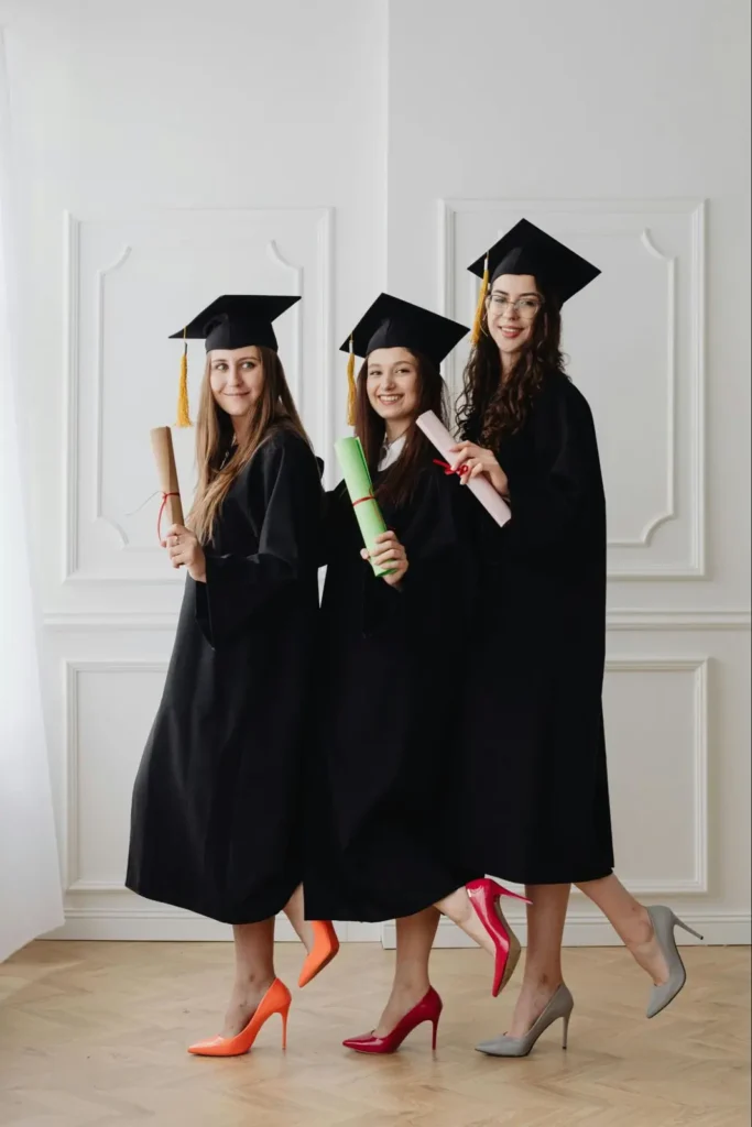 Group of graduates in vibrant heels and gowns holding diplomas, adding a creative touch to graduation photos.