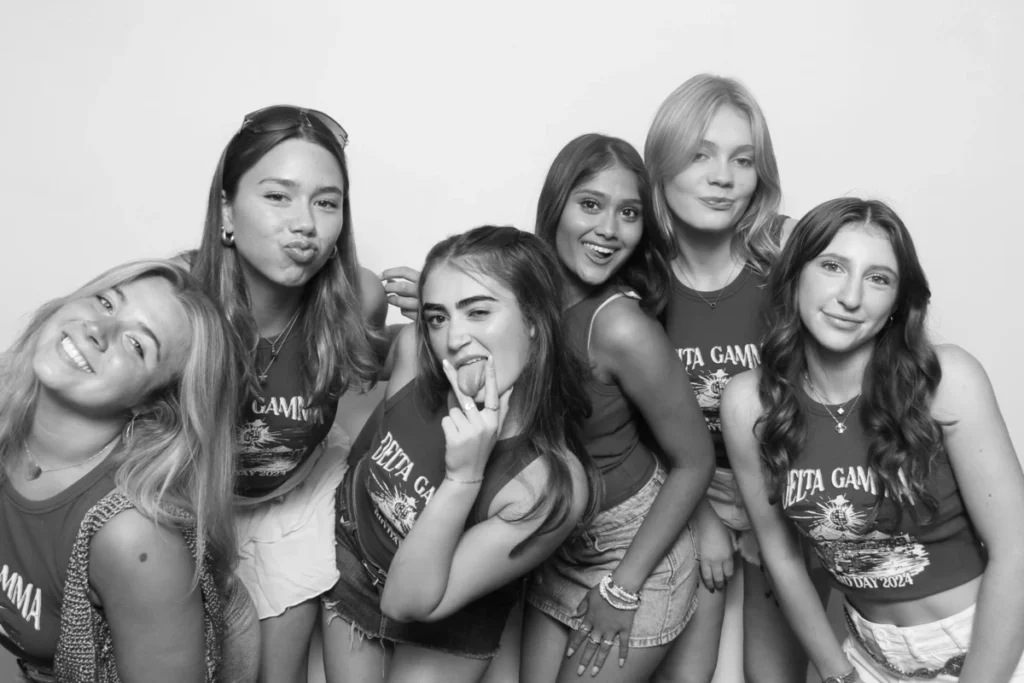 Group of young women in matching outfits striking fun and playful poses in a photo booth.