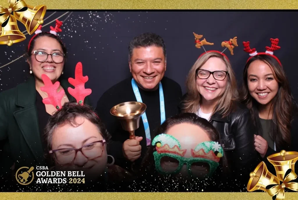 Group photo at CSBA Golden Bell Awards 2024 with festive reindeer headbands and holiday props against sparkly backdrop