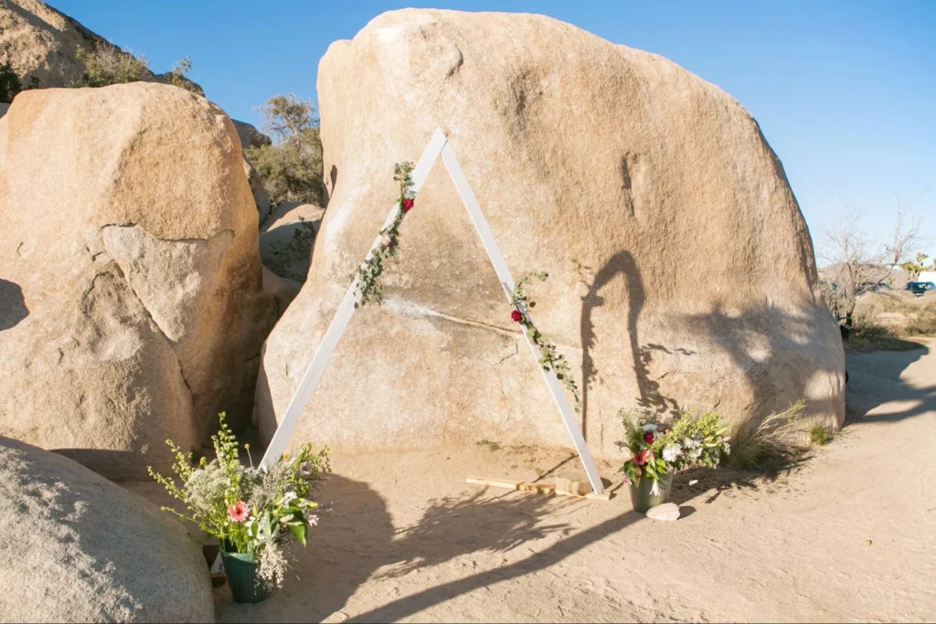 Minimalist triangle wedding arch with floral decor in a desert setting.