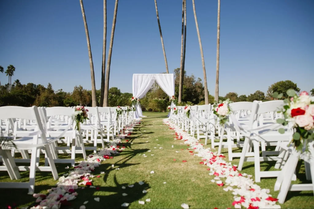 Outdoor wedding setup with white chairs and floral aisle.