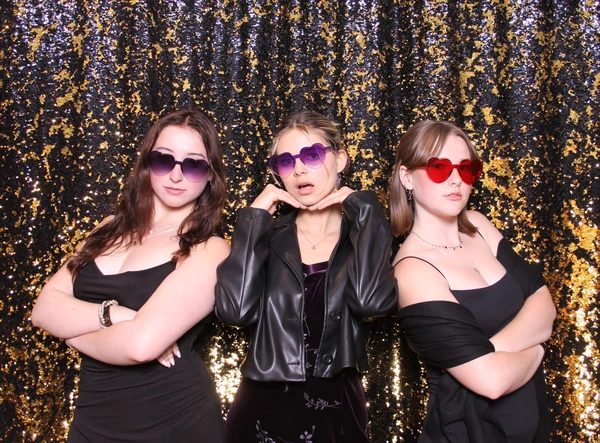 Three women posing stylishly in heart-shaped sunglasses against a sparkling gold and black sequin backdrop, showcasing the fun and elegance of a premium photo booth experience.