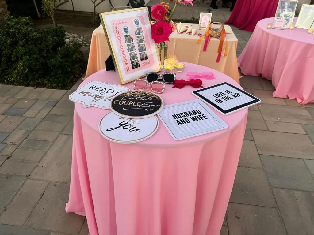 Photo booth props displayed on pink table at wedding.