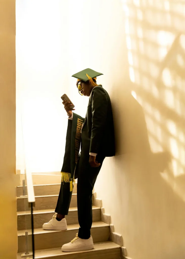 Solo graduation photo idea with a formal pose leaning against a brick wall, holding a diploma