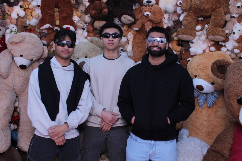 Three individuals pose confidently in front of a backdrop filled with plush teddy bears.