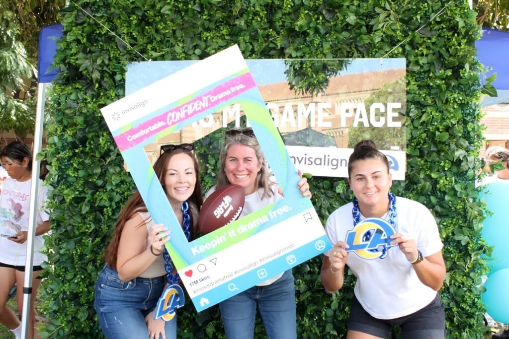 Three women pose with a football and a playful DIY photo booth frame.