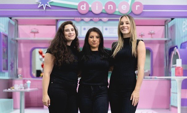 Three women posing at a corporate event with a themed backdrop