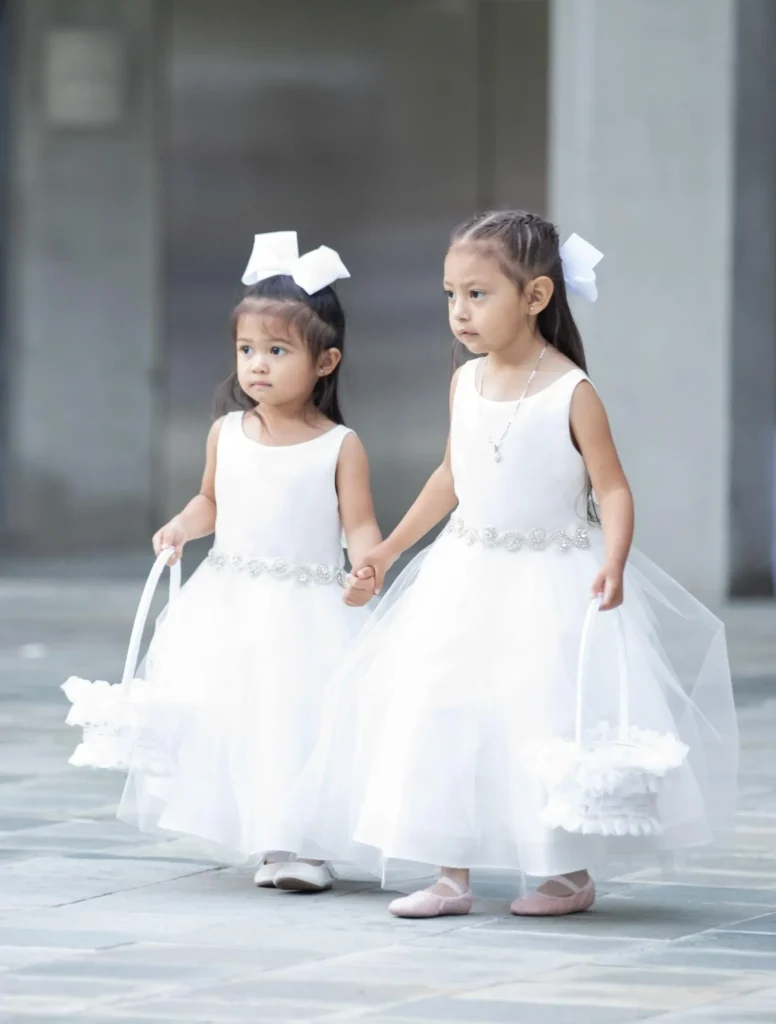 Two flower girls in white dresses holding baskets of petals.