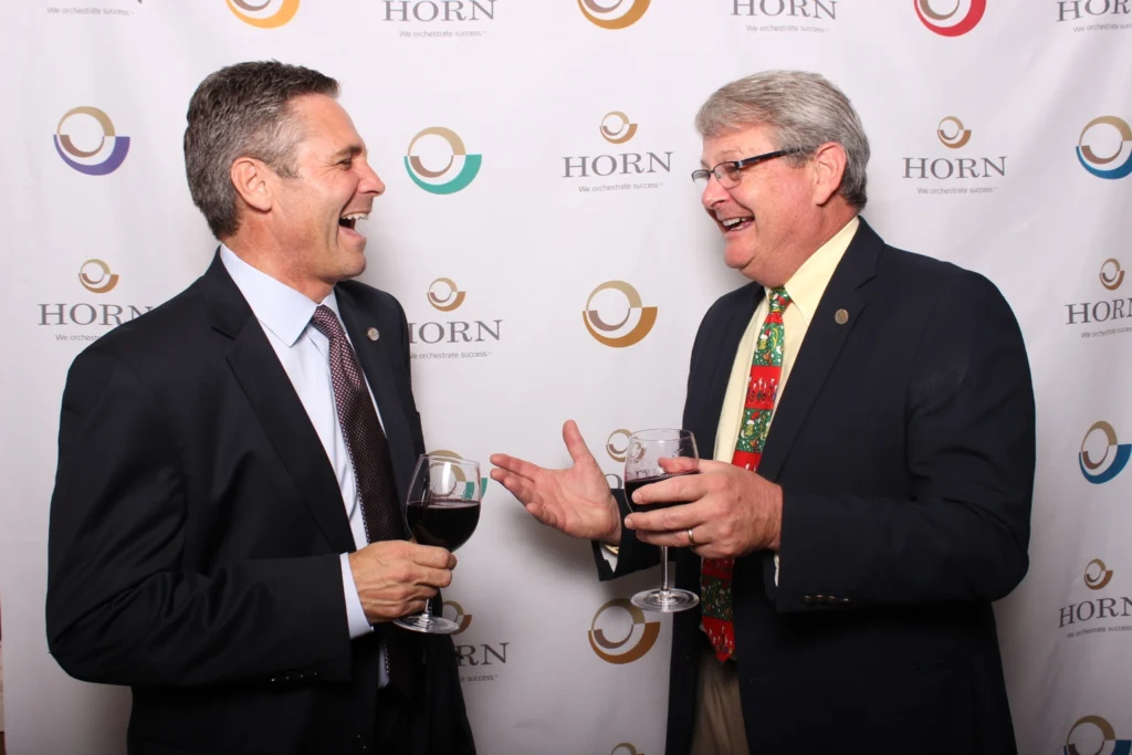 Two professionals laughing and networking at a corporate event with wine glasses in hand.