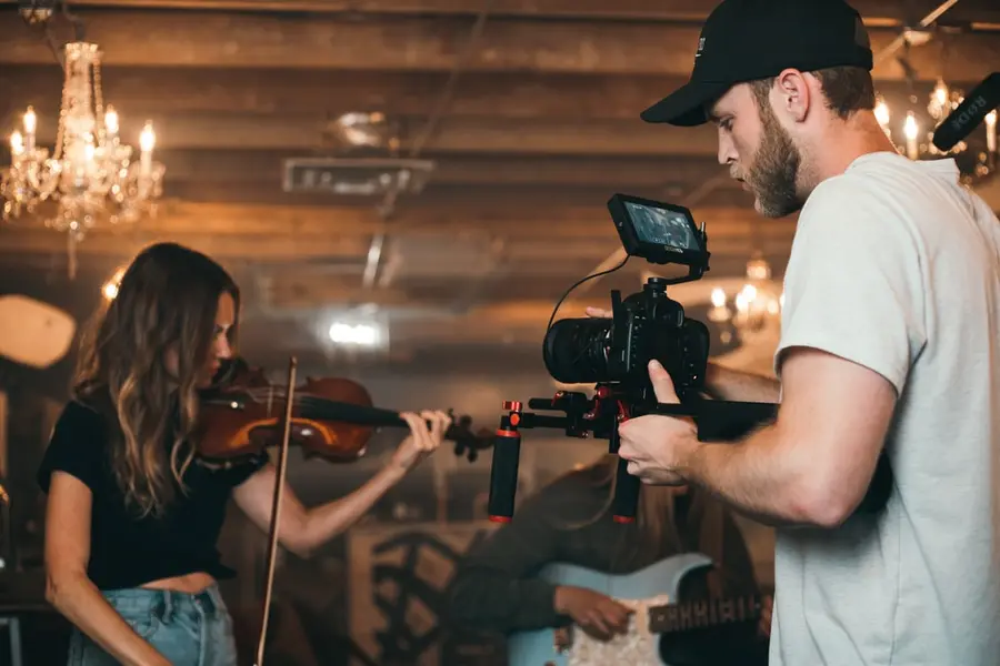 Videographer filming a musician playing the violin in a rustic setting.