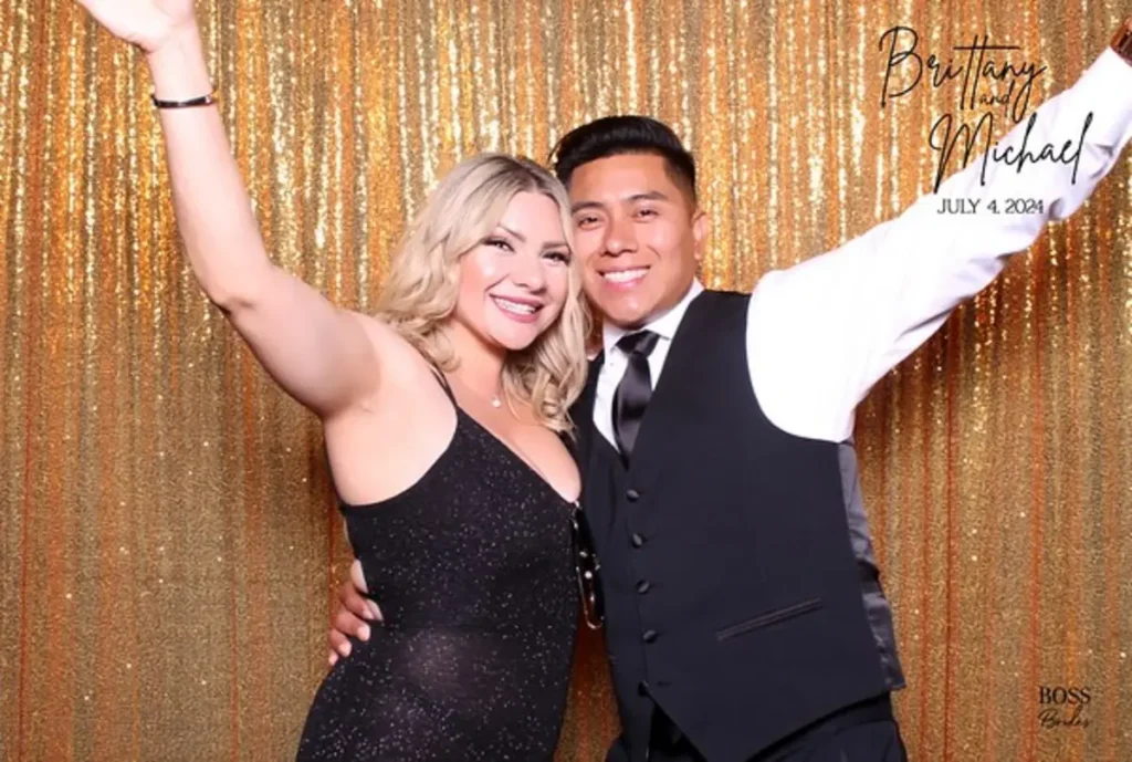 Wedding couple posing energetically against gold sequin backdrop, bride in black dress and groom in vest