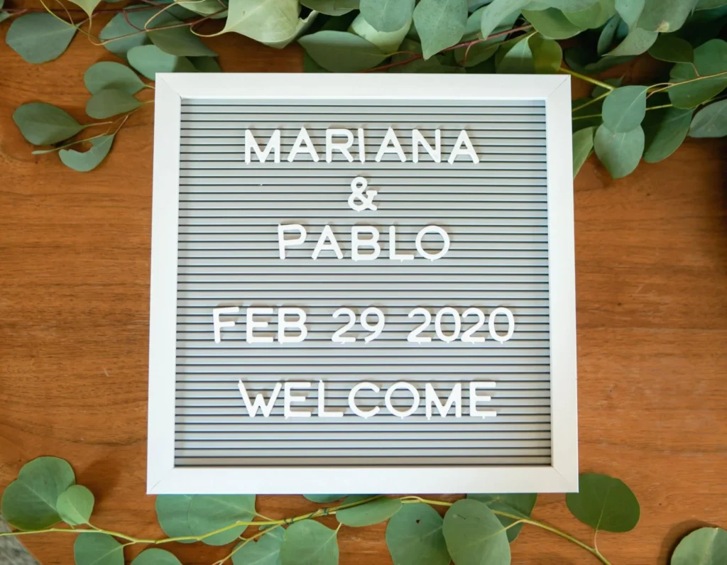 Welcome sign with names and wedding date, framed by greenery.