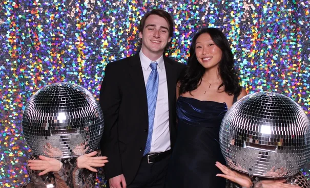 Couple posing with disco ball props in a colorful photo booth setup at a party.