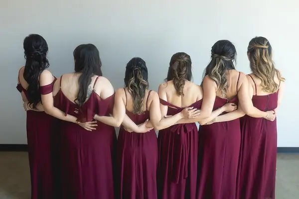 Bridesmaids in burgundy dresses posing with backs turned showing matching hairstyles