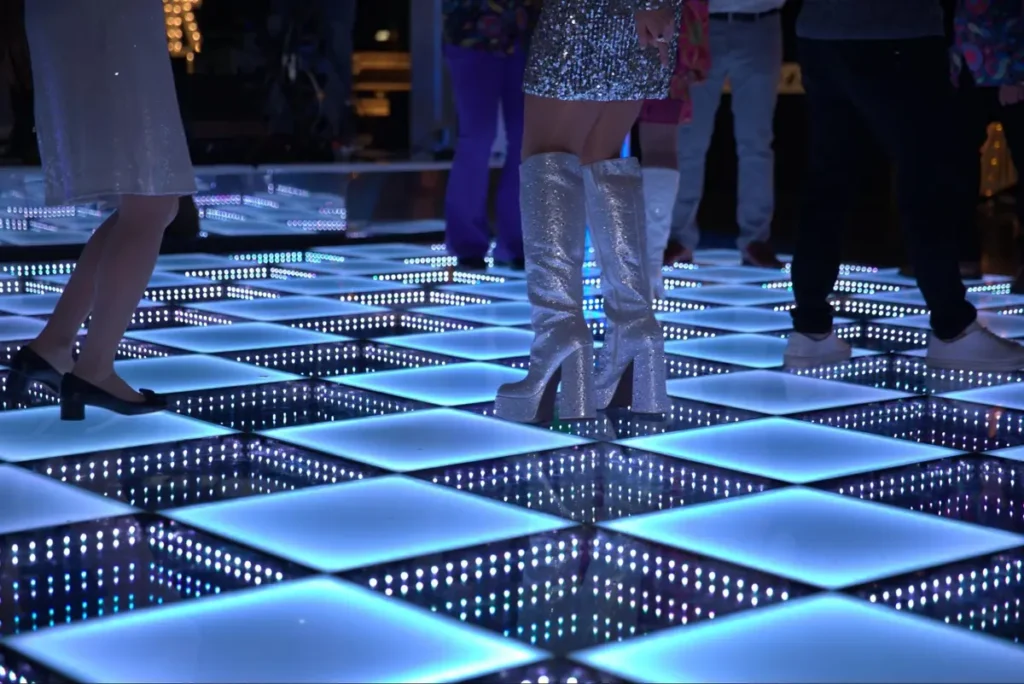 Close-up of illuminated LED dance floor panels with glittery boots showing scale and lighting effects for event planning