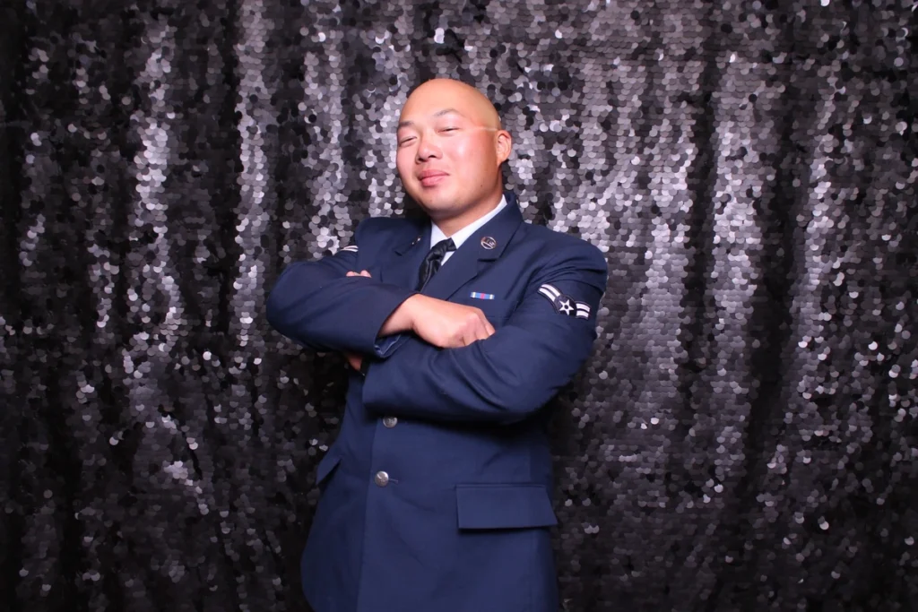 Confident military pose in photo booth, serviceman in Air Force dress uniform against silver sequin backdrop