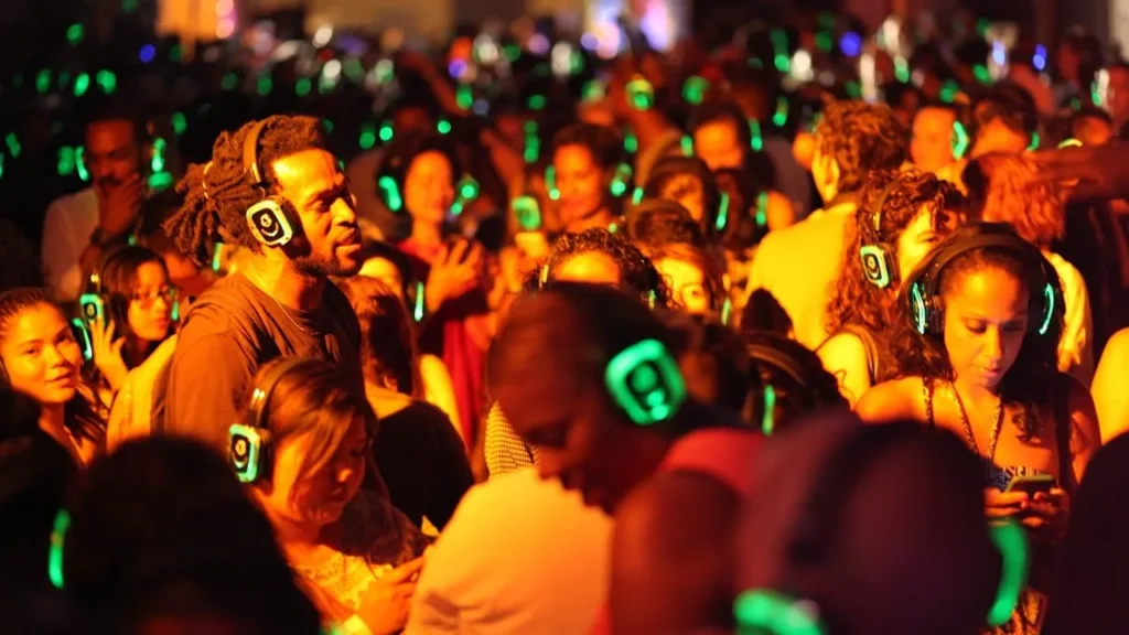 Crowded silent disco dance floor with participants wearing glowing green wireless headphones in warm ambient lighting