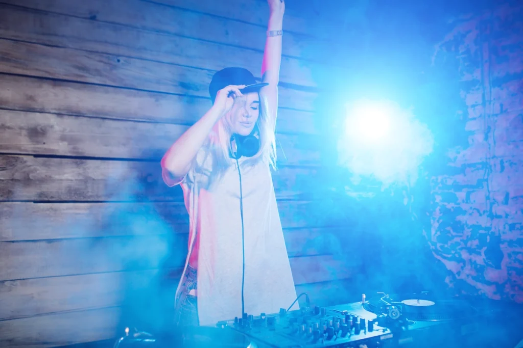 Female DJ performing at silent disco event, wearing headphones and baseball cap with dramatic blue lighting